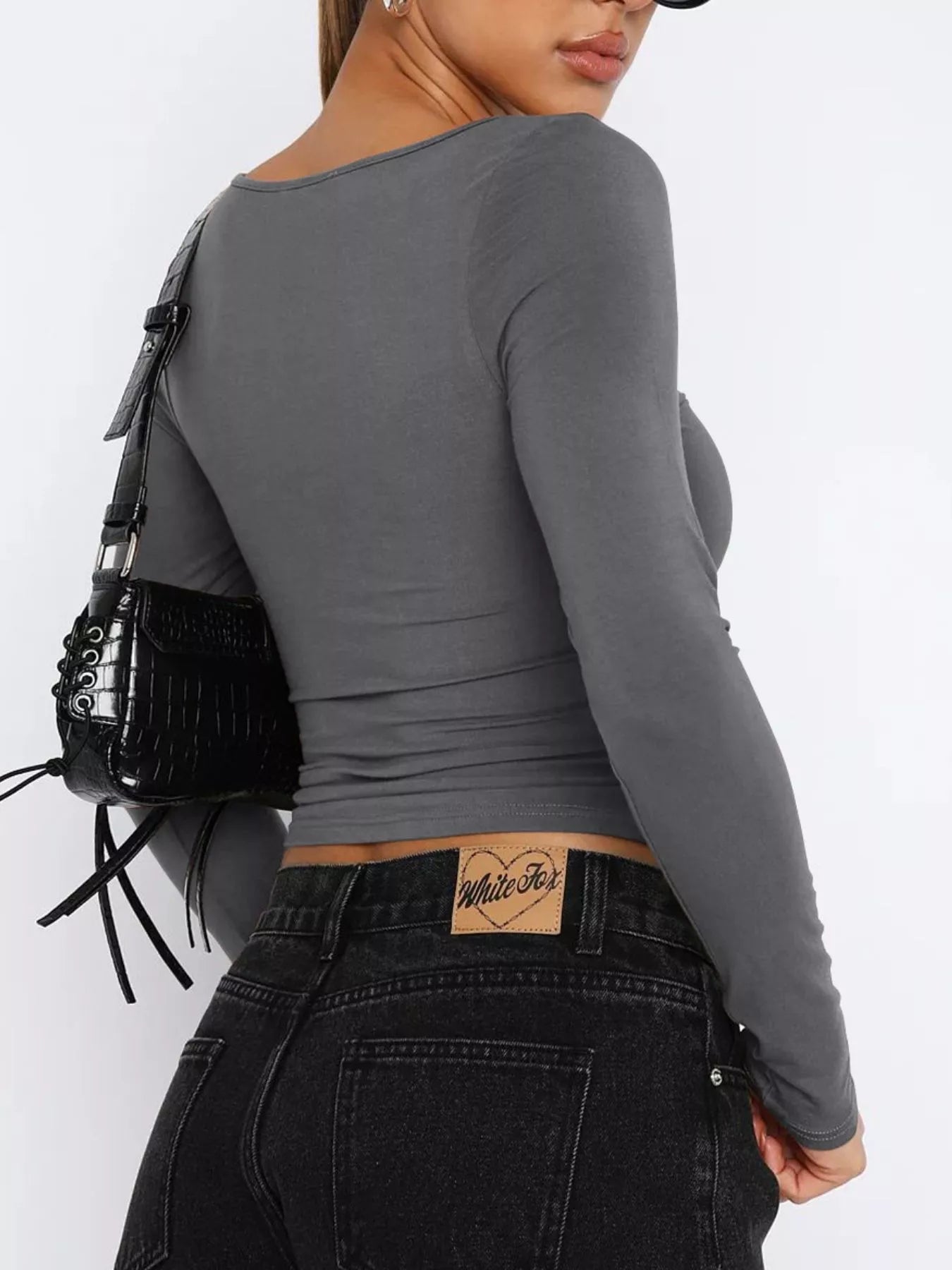 Woman wearing a trendy fitted tee in gray, paired with high-waisted black jeans and a stylish handbag
