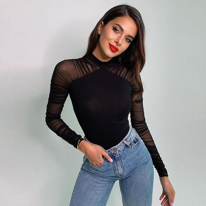 A woman modeling a black long-sleeve mock neck top with sheer mesh sleeves and shoulder panels, paired with light blue jeans, against a plain light gray background.