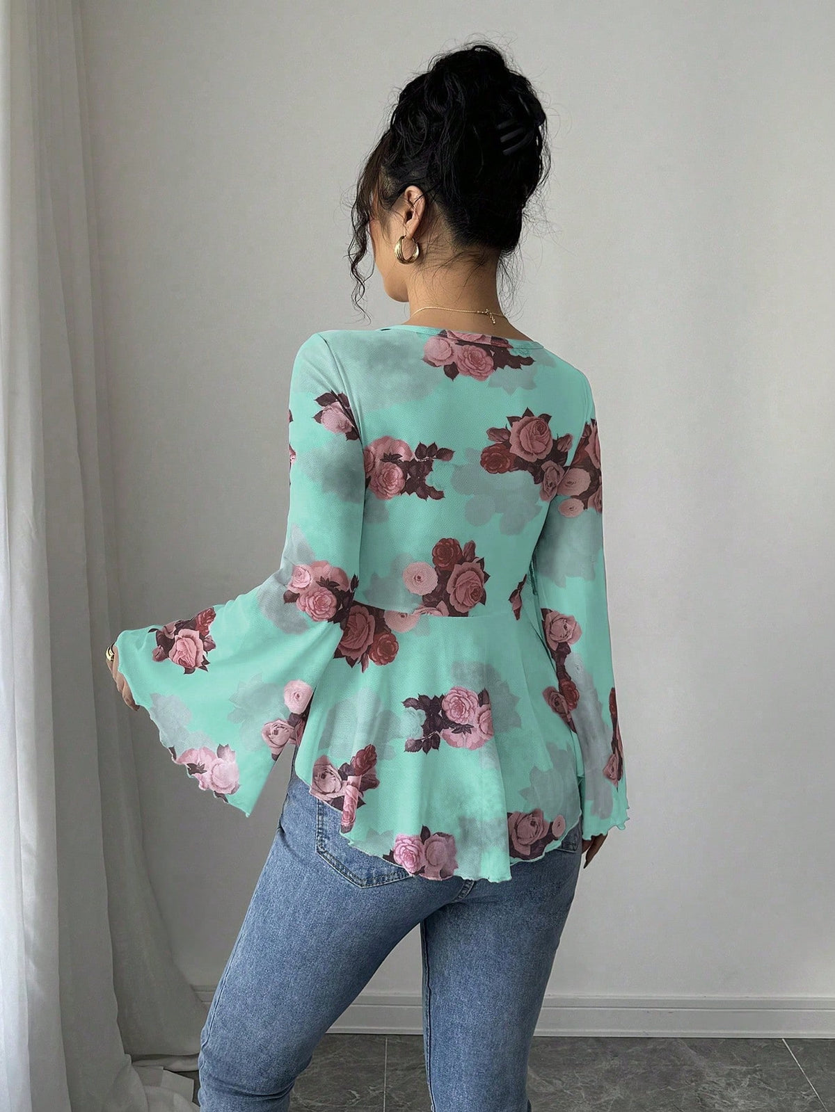 Back view of Person wearing a floral bell-sleeve top and jeans against a neutral background