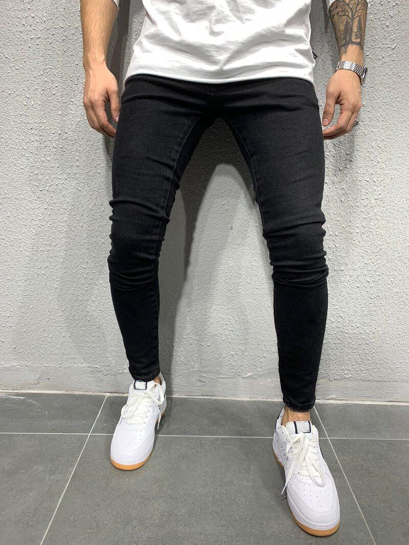 Person wearing black skinny jeans and white sneakers against a gray wall.
