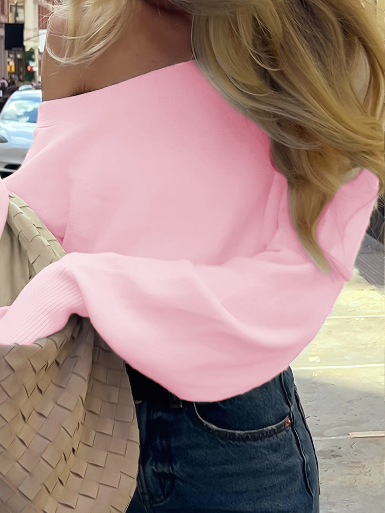 A close-up lifestyle shot of a woman wearing a light pink off-the-shoulder knit sweater and dark blue jeans, carrying a woven beige shoulder bag.
