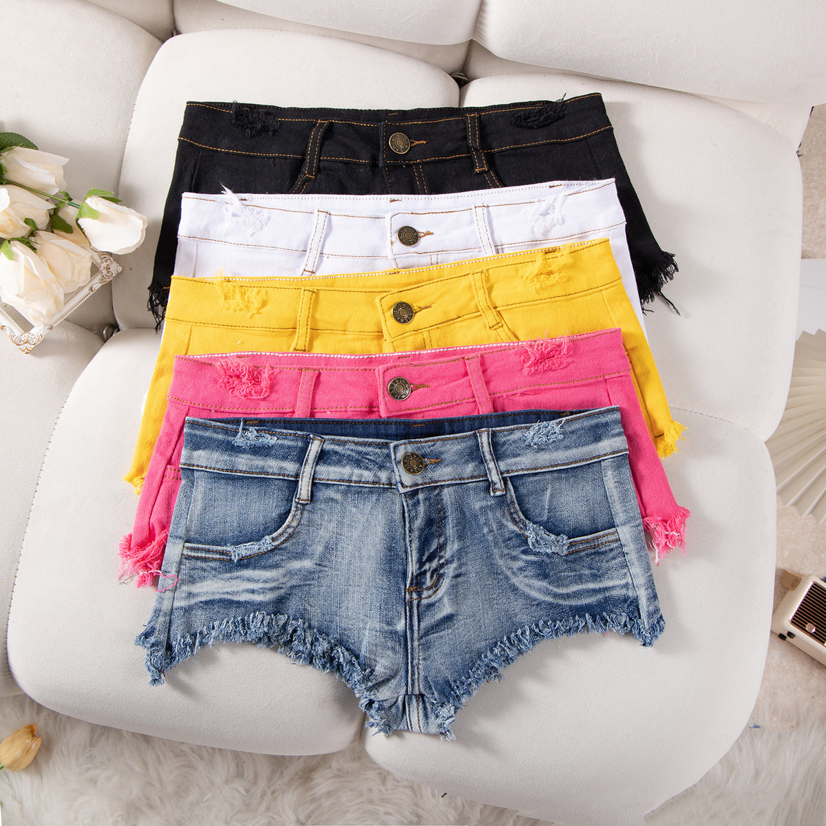 Stack of ultra-low-rise denim shorts in black, white, yellow, pink, and blue washes