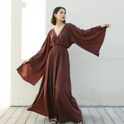 Model wearing a flowing batwing sleeve maxi dress with elegant drape and wide sleeves in soft natural light