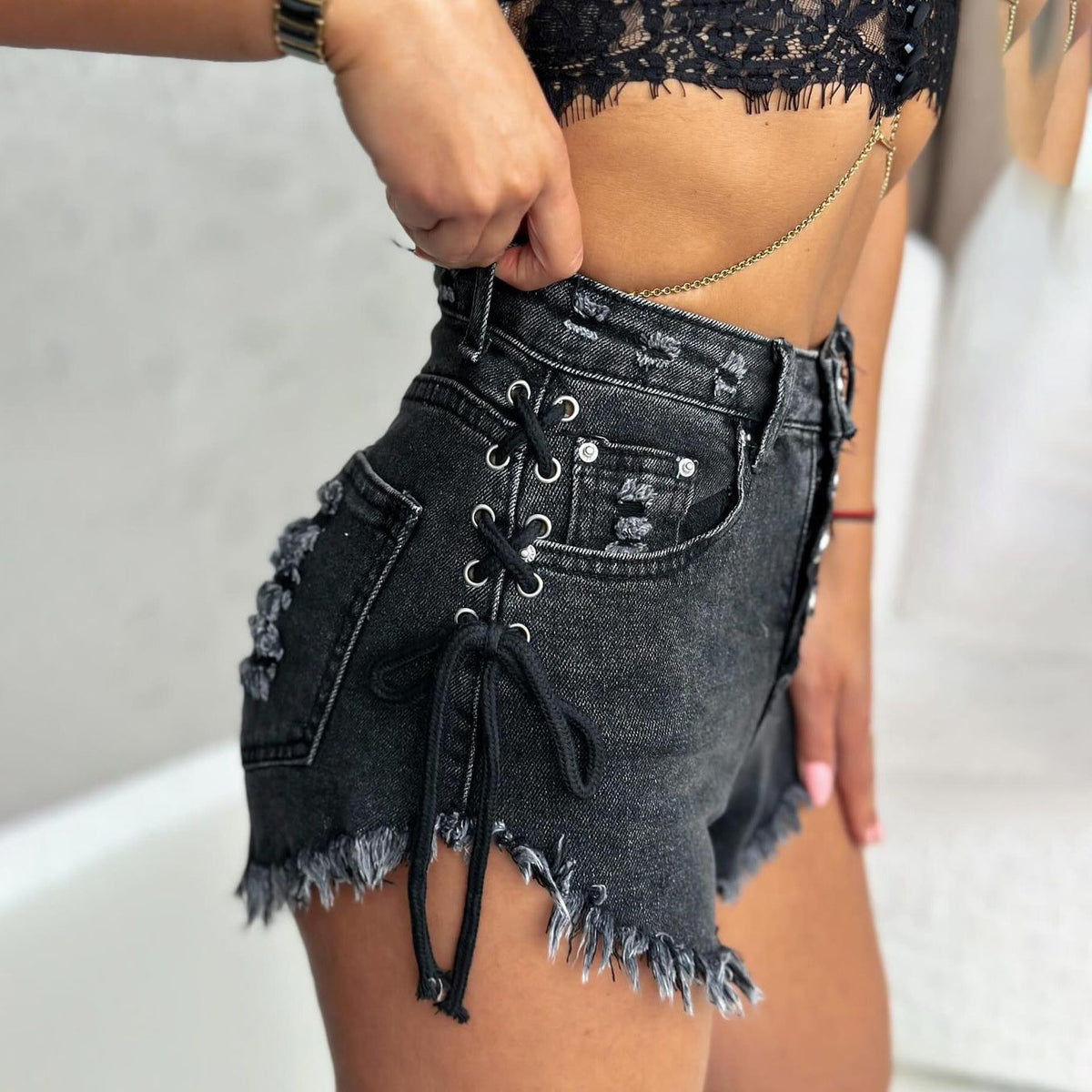 Black high-waisted denim shorts with lace-up sides and frayed hem