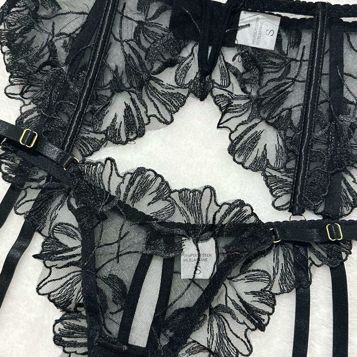 Black sheer floral lace garter belt with adjustable elastic straps and gold-tone buckles.