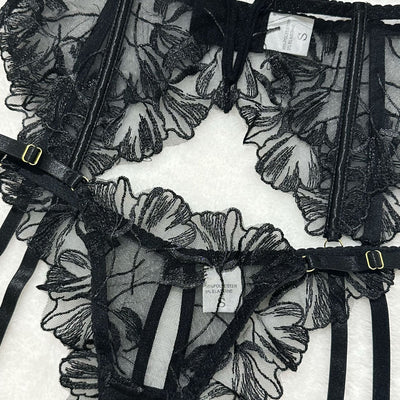 Black sheer floral lace garter belt with adjustable elastic straps and gold-tone buckles.