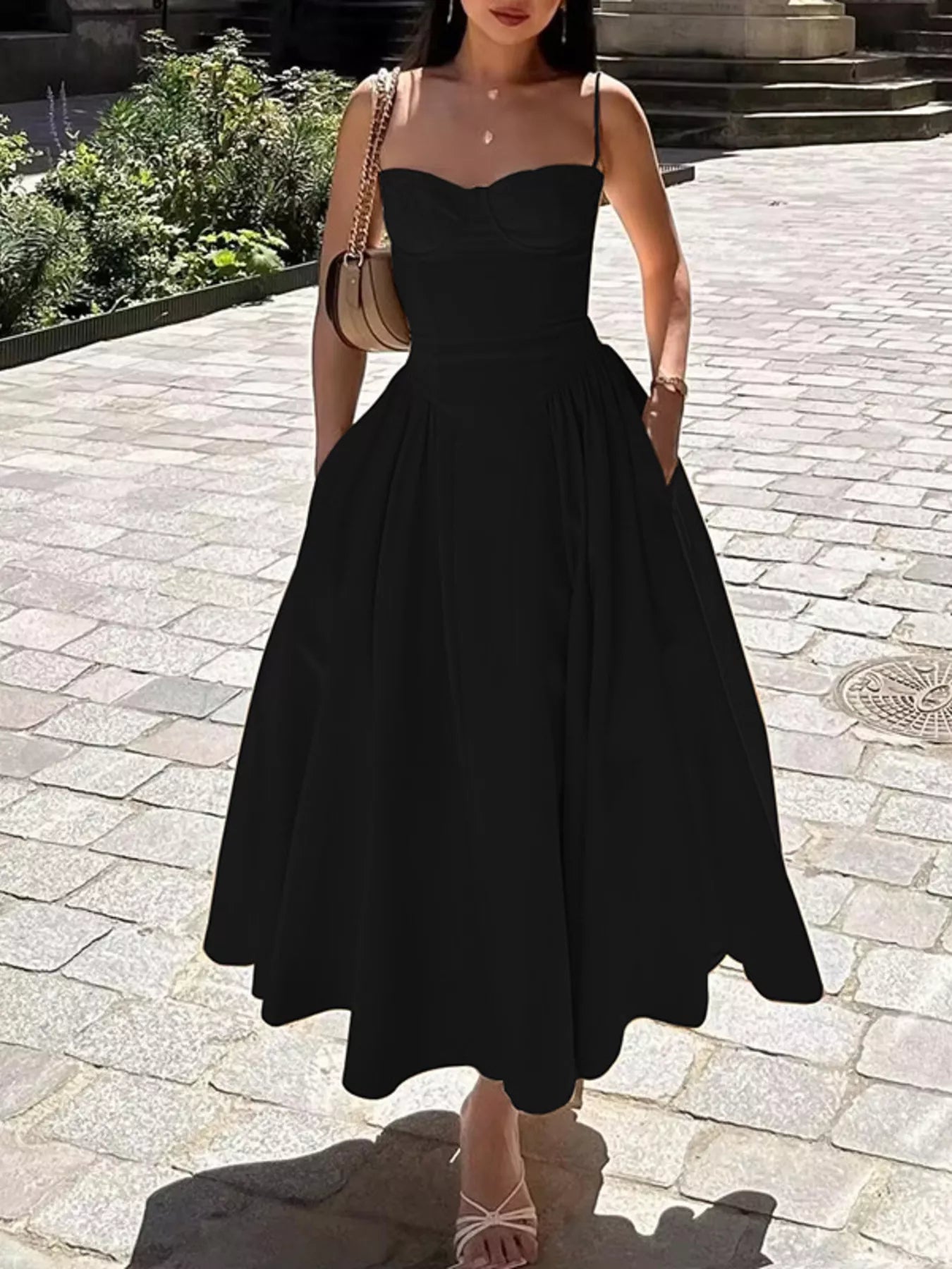 Woman wearing a black dress standing on a stone pavement.