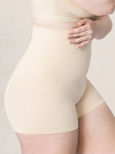 Close-up of a model wearing high-waisted beige shapewear shorts with a subtle tonal swirl pattern, paired with a matching beige top against a light beige studio background.