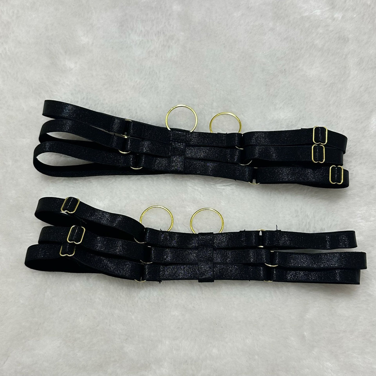 Black garter belt straps with adjustable buckles and metal rings, laid flat