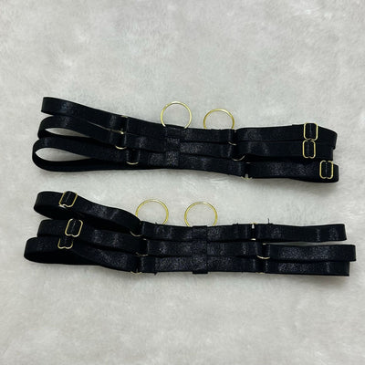 Black garter belt straps with adjustable buckles and metal rings, laid flat