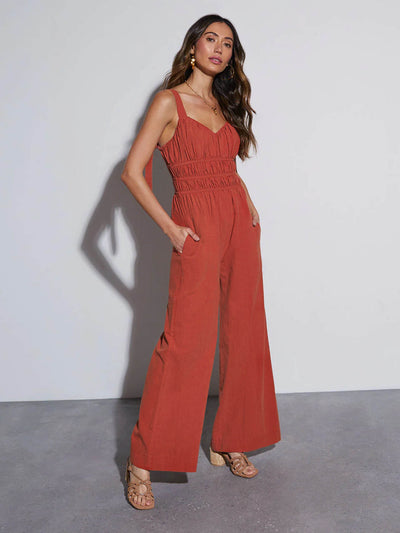 Rust-red wide-leg jumpsuit with smocked waist and side pockets, sleeveless V-neck
