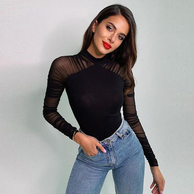 A woman modeling a black long-sleeve mock neck top with sheer mesh sleeves and shoulder panels, paired with light blue jeans, against a plain light gray background.