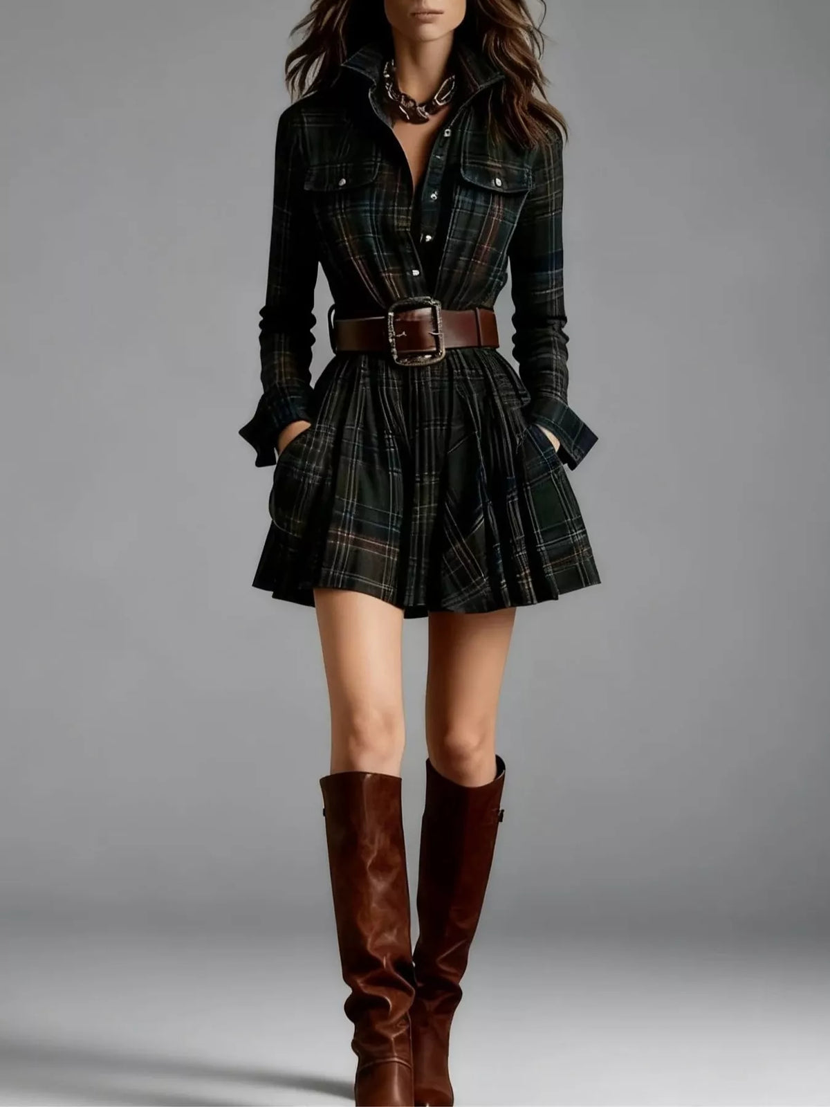 Woman wearing a plaid dress with a belt and brown knee-high boots on a gray background