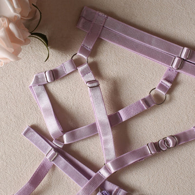 Lilac garter belt straps with metal adjusters and elastic bands in a crisscross layout