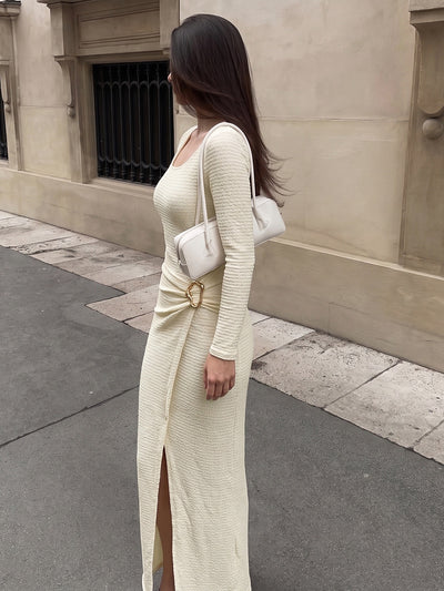 Cream knit maxi dress with long sleeves, side slit, gathered hip and gold metal accent.