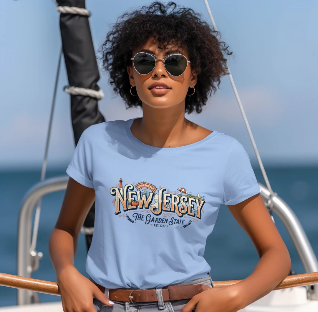 A woman wearing a light blue crewneck t-shirt with a 'New Jersey The Garden State' graphic, standing on a boat with the ocean in the background.