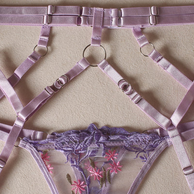 Lilac garter belt with crisscross straps and metal adjusters beneath a lace thong