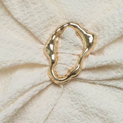 Gold oval metal accent with gathered stitching on cream knit dress.