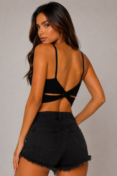 Woman wearing a black open-back top and black shorts on a gray background