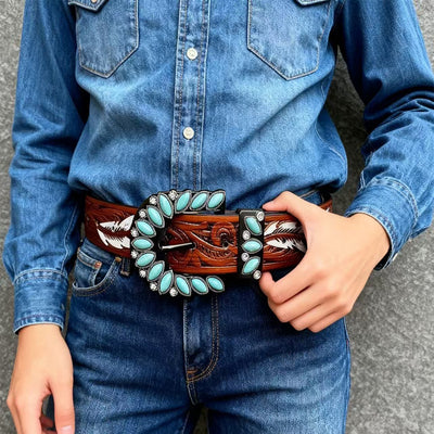 Western feather belt close-up with turquoise stone border and engraved buckle over denim